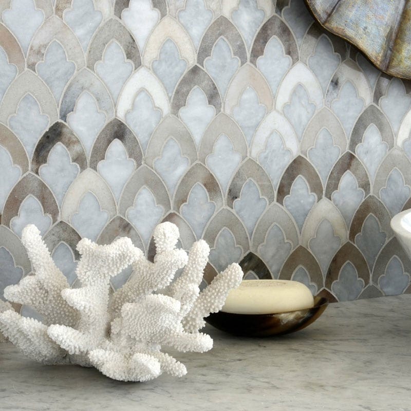 Marble mosaic tile backsplash with a scalloped fan pattern in shades of gray, beige, and white, styled with a white coral ornament and a soap dish on a marble countertop.