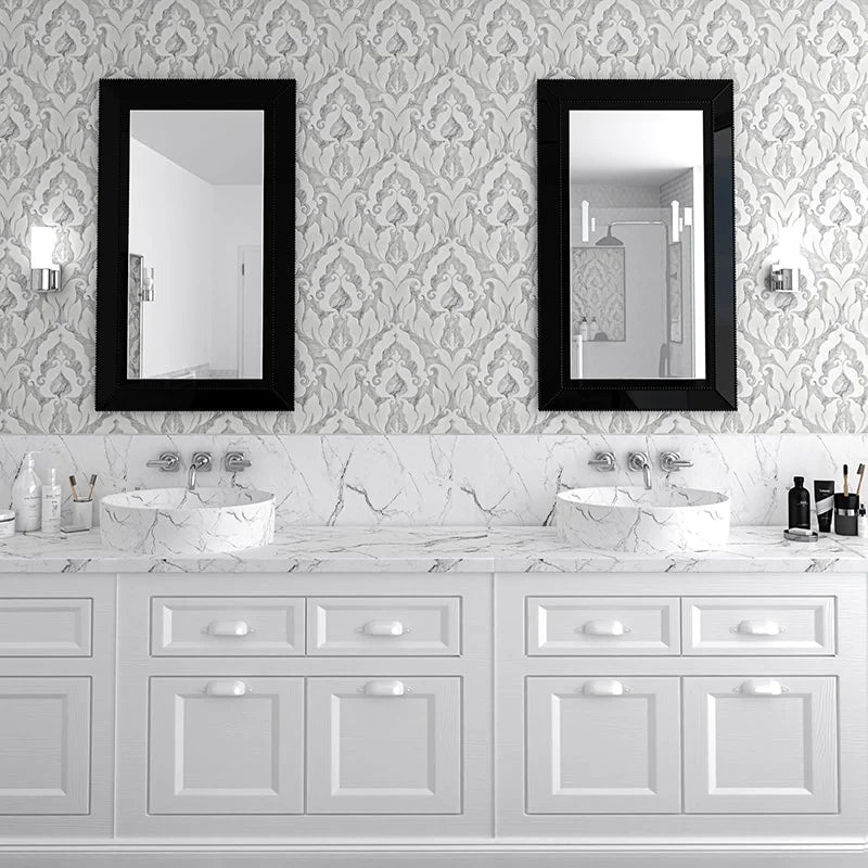 A double-sink bathroom vanity with white cabinets, a white marble countertop, and two black-framed rectangular mirrors mounted on a gray damask-patterned wall.