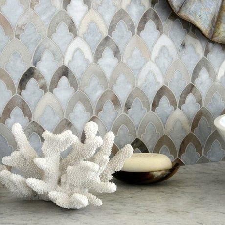 Marble mosaic tile backsplash with a scalloped fan pattern in shades of gray, beige, and white, styled with a white coral ornament and a soap dish on a marble countertop.