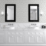 A double-sink bathroom vanity with white cabinets, a white marble countertop, and two black-framed rectangular mirrors mounted on a gray damask-patterned wall.