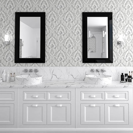 A double-sink bathroom vanity with white cabinets, a white marble countertop, and two black-framed rectangular mirrors mounted on a gray damask-patterned wall.